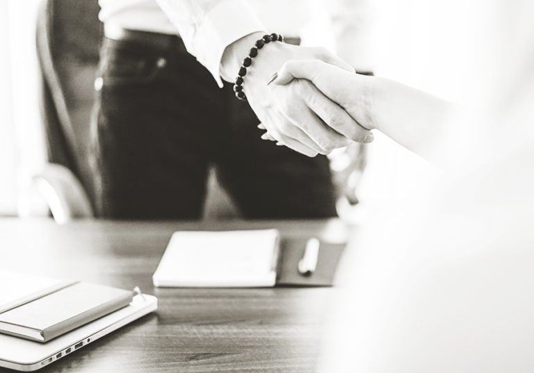 A man and a woman shaking hands over an office desk.